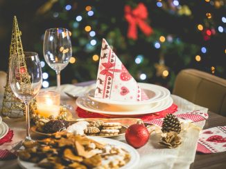Beautifully set Christmas table with decorations, food, and drinks under festive lights.