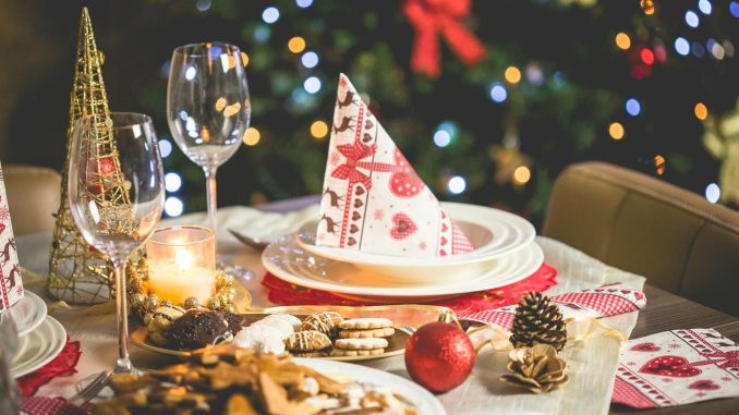 Beautifully set Christmas table with decorations, food, and drinks under festive lights.