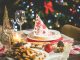 Beautifully set Christmas table with decorations, food, and drinks under festive lights.