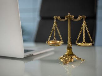 Golden justice scales on a desk beside a laptop, symbolizing law and balance.