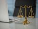 Golden justice scales on a desk beside a laptop, symbolizing law and balance.