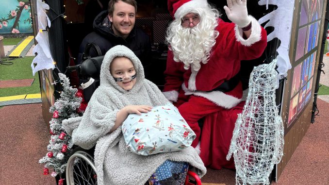 A young patient in a wheelchair sitting in Santa's grotto with Santa.