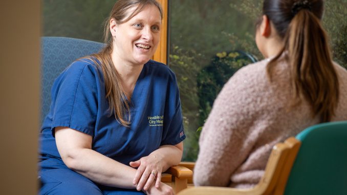A City Hospice member wearing a blue uniform talking to a patient.