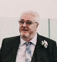 A photo of a man with glasses wearing a suit on a wedding day with a pastel blue tie.