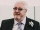 A photo of a man with glasses wearing a suit on a wedding day with a pastel blue tie.