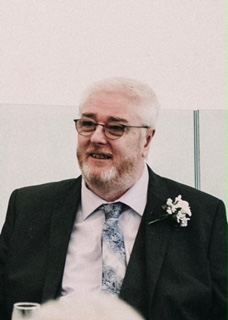 A photo of a man with glasses wearing a suit on a wedding day with a pastel blue tie.