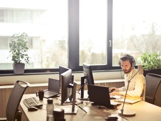 A person sat at an office desk in front of multiple monitors.