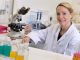 Dr Emma Saunders wearing a white lab coat, sat at a desk in a lab next to a microscope.