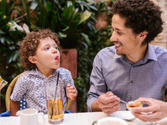 Father and son share a joyful moment while dining outdoors, capturing playful expressions.