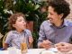 Father and son share a joyful moment while dining outdoors, capturing playful expressions.