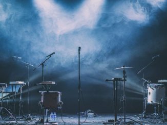 Musical instruments and microphones on a stage with blue spotlights and thick haze