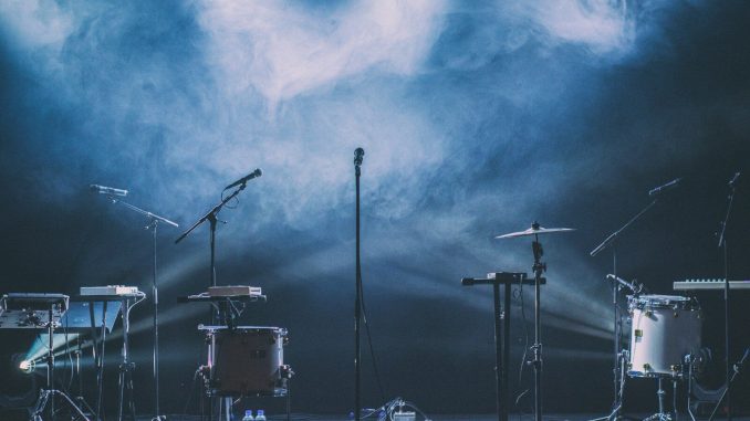 Musical instruments and microphones on a stage with blue spotlights and thick haze